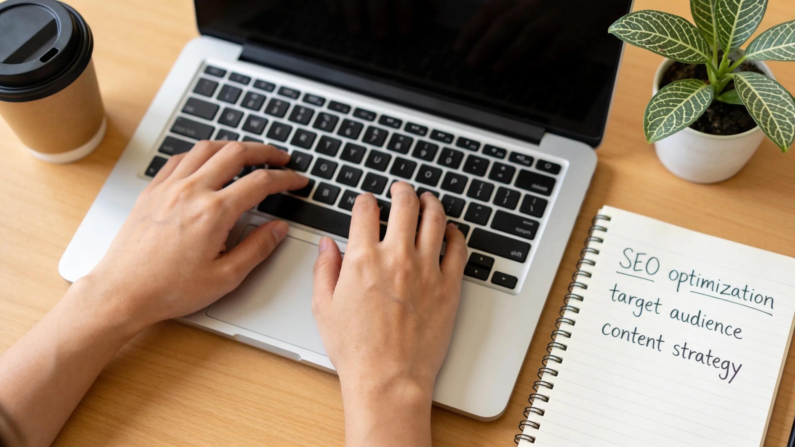 Hands typing on a laptop while researching keywords with a notepad Hands typing on a laptop while researching keywords with a notepad