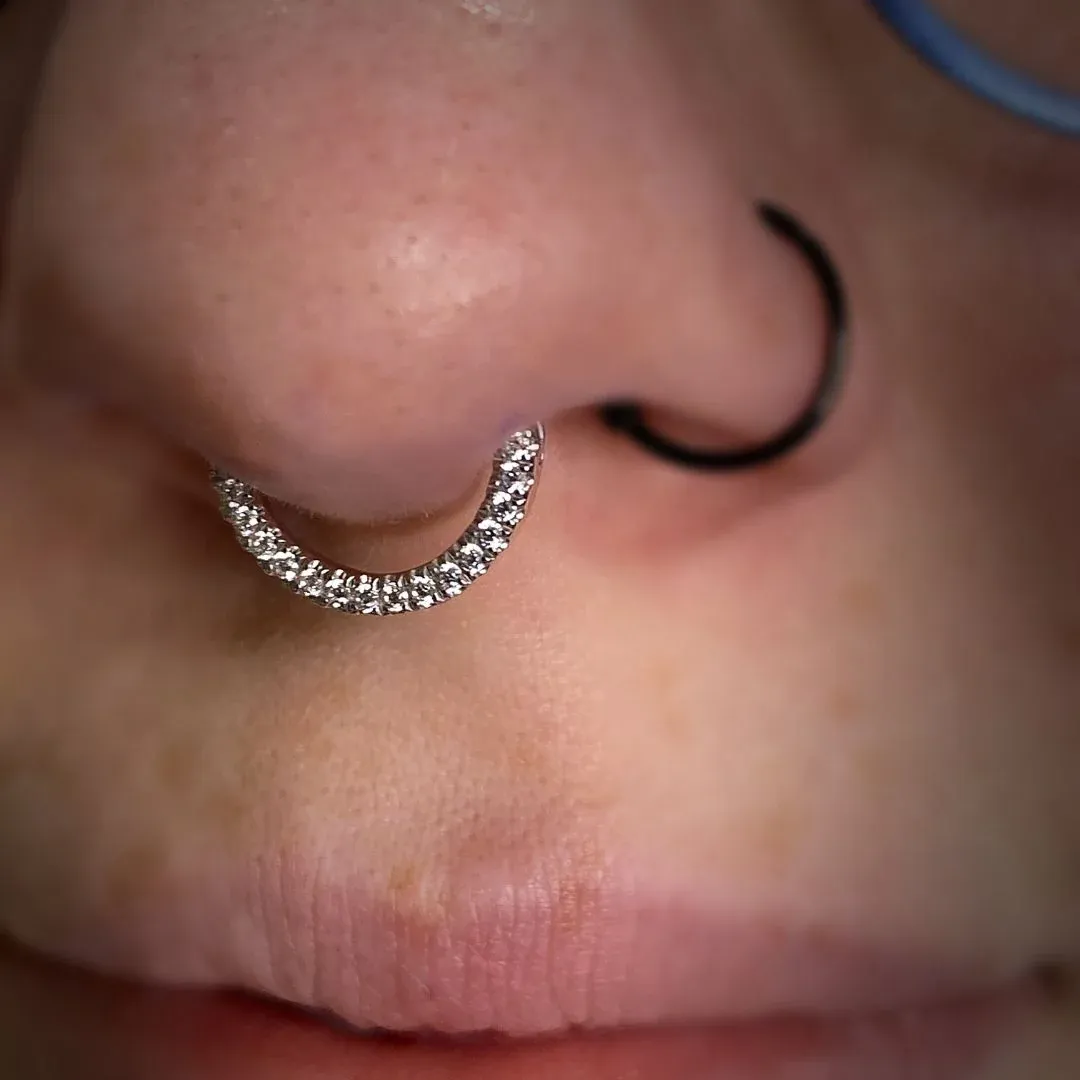 Close-up of a nose featuring a sparkling paved diamond septum clicker hoop paired with a sleek black nostril ring.