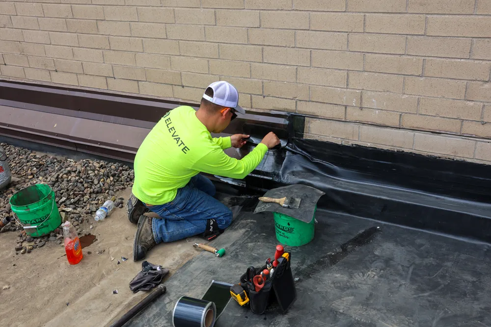 Construction worker applying roofing material on a building's edge