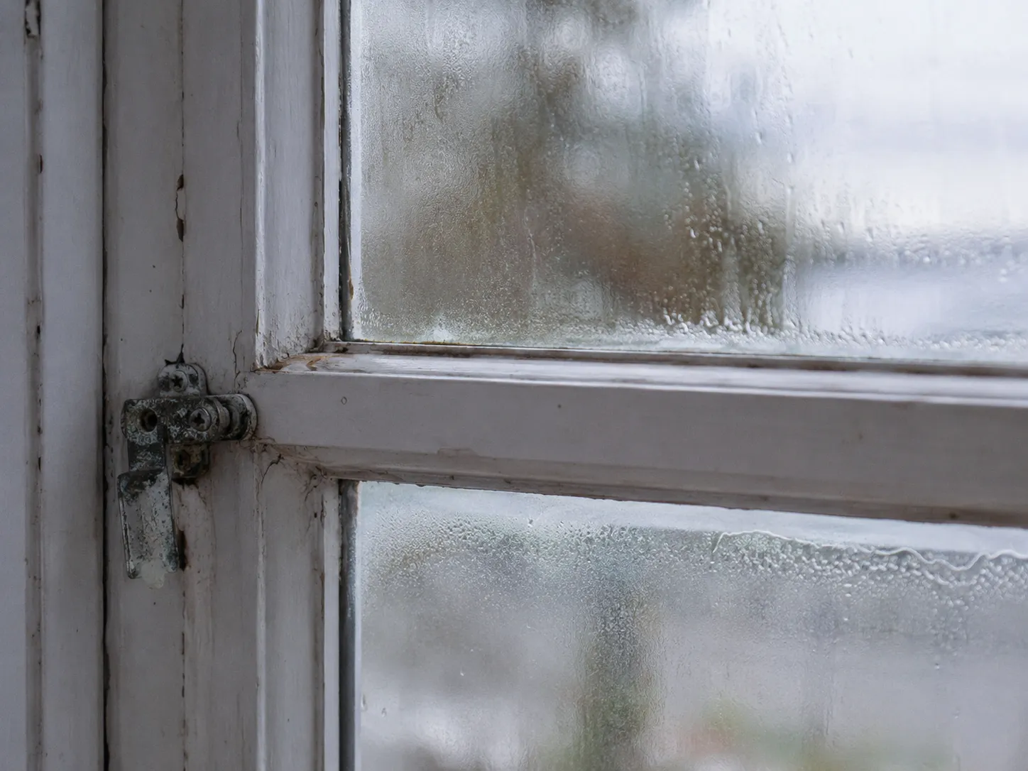 Older coastal home window showing condensation, worn seals, and weathering