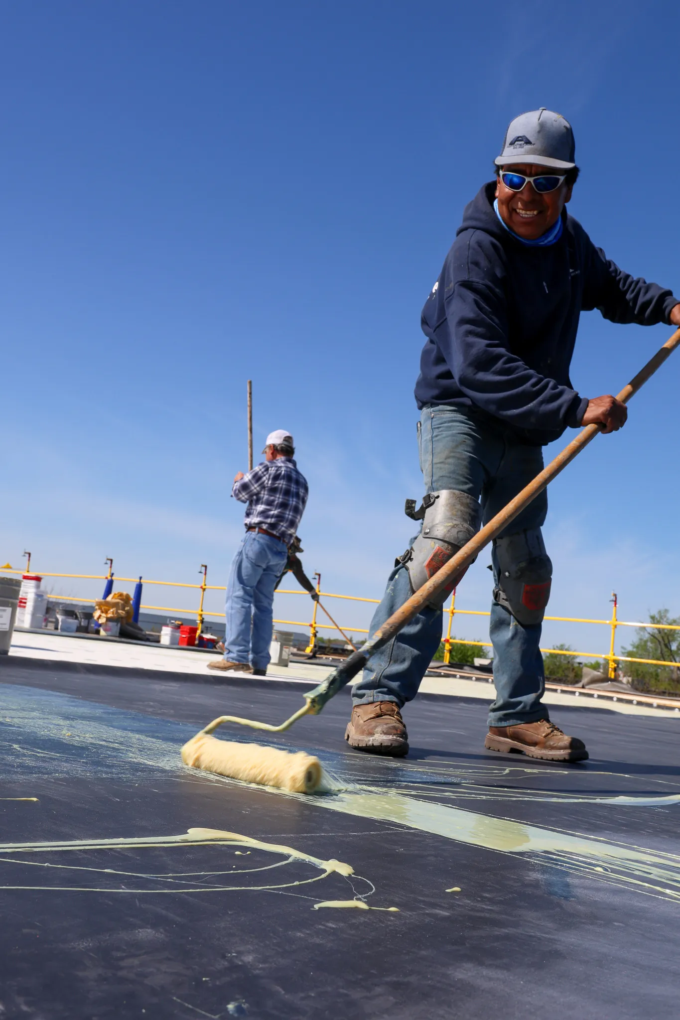 Two men applying paint on a rooftop under a clear blue sky