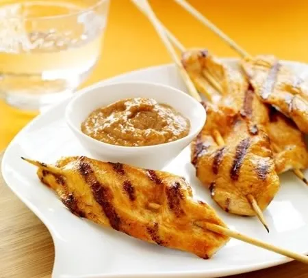 Grilled chicken skewers served with peanut sauce on a white plate