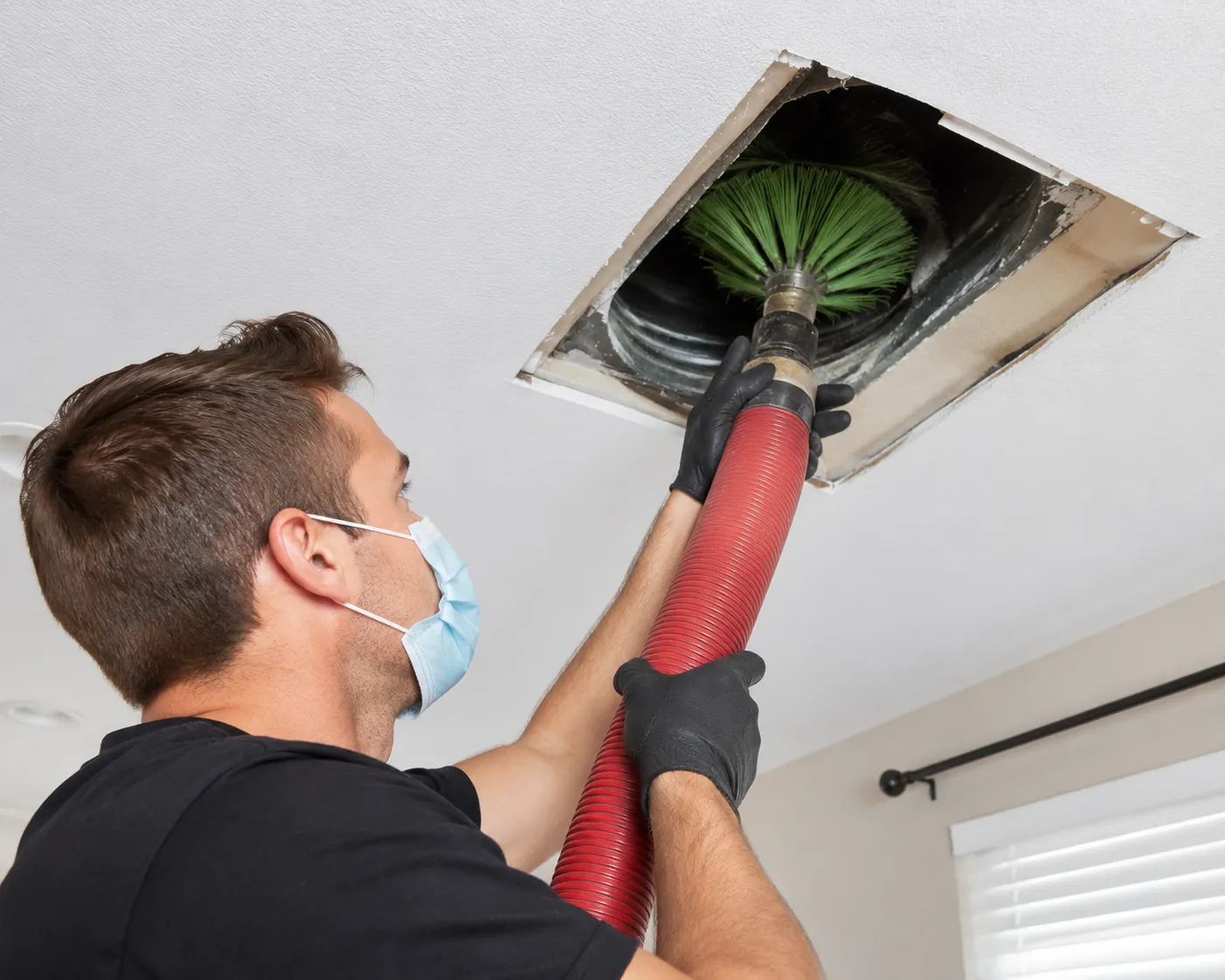 Technician cleaning an air conditioning duct with professional HVAC equipment inside a home.