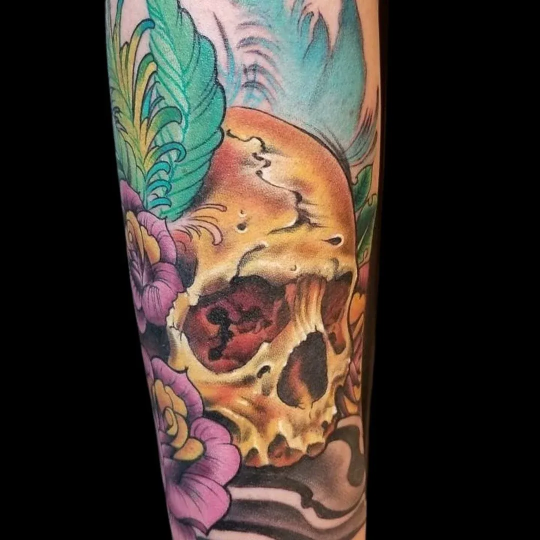 Colorful skull tattoo featuring purple roses, green feathers, and vibrant shading by a Club Tattoo Las Vegas artist.