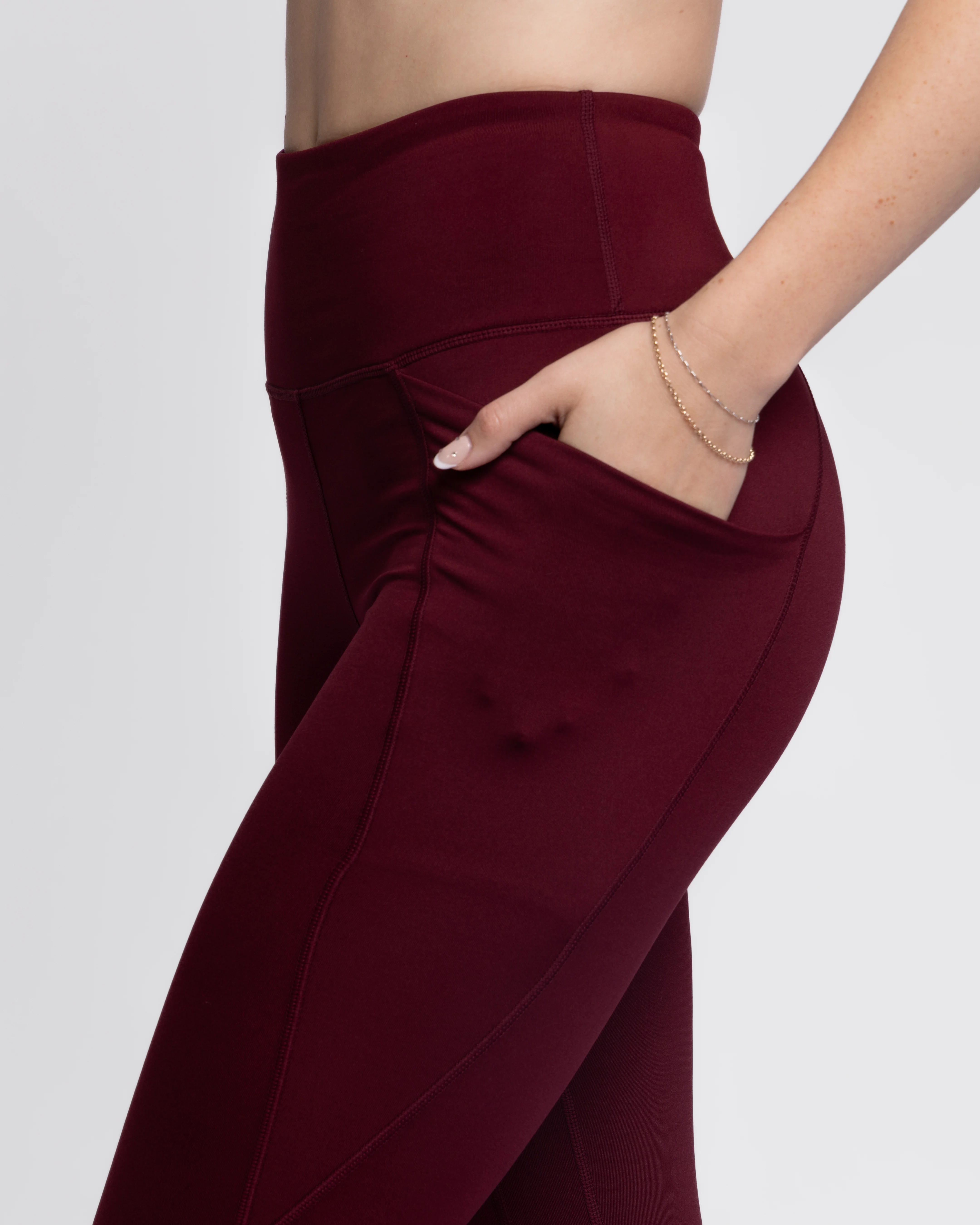 Close-up side profile of a woman showing the deep, secure side pocket of high-waisted maroon activewear leggings.