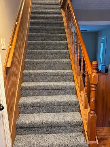 Carpeted staircase with gray carpeting and wooden handrail, illustrating a durable and stylish flooring option for home interiors.