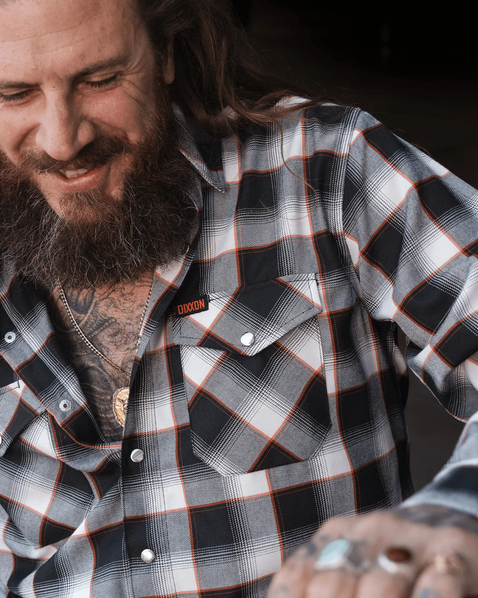 Bearded guy wearing The Shovel 2.0 flannel featuring black, white, and orange plaid with pearl snap buttons.