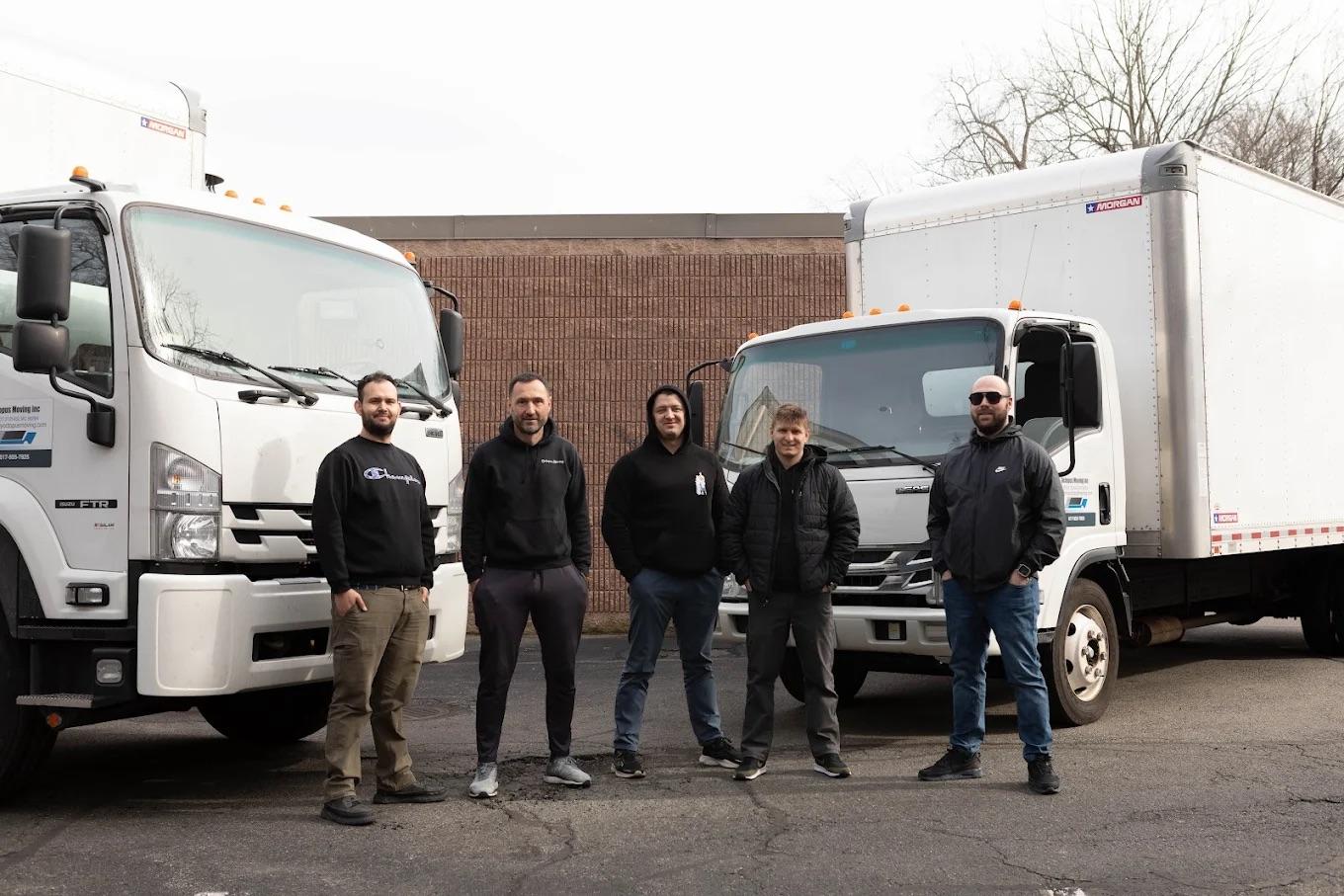 Team of movers standing beside two moving trucks