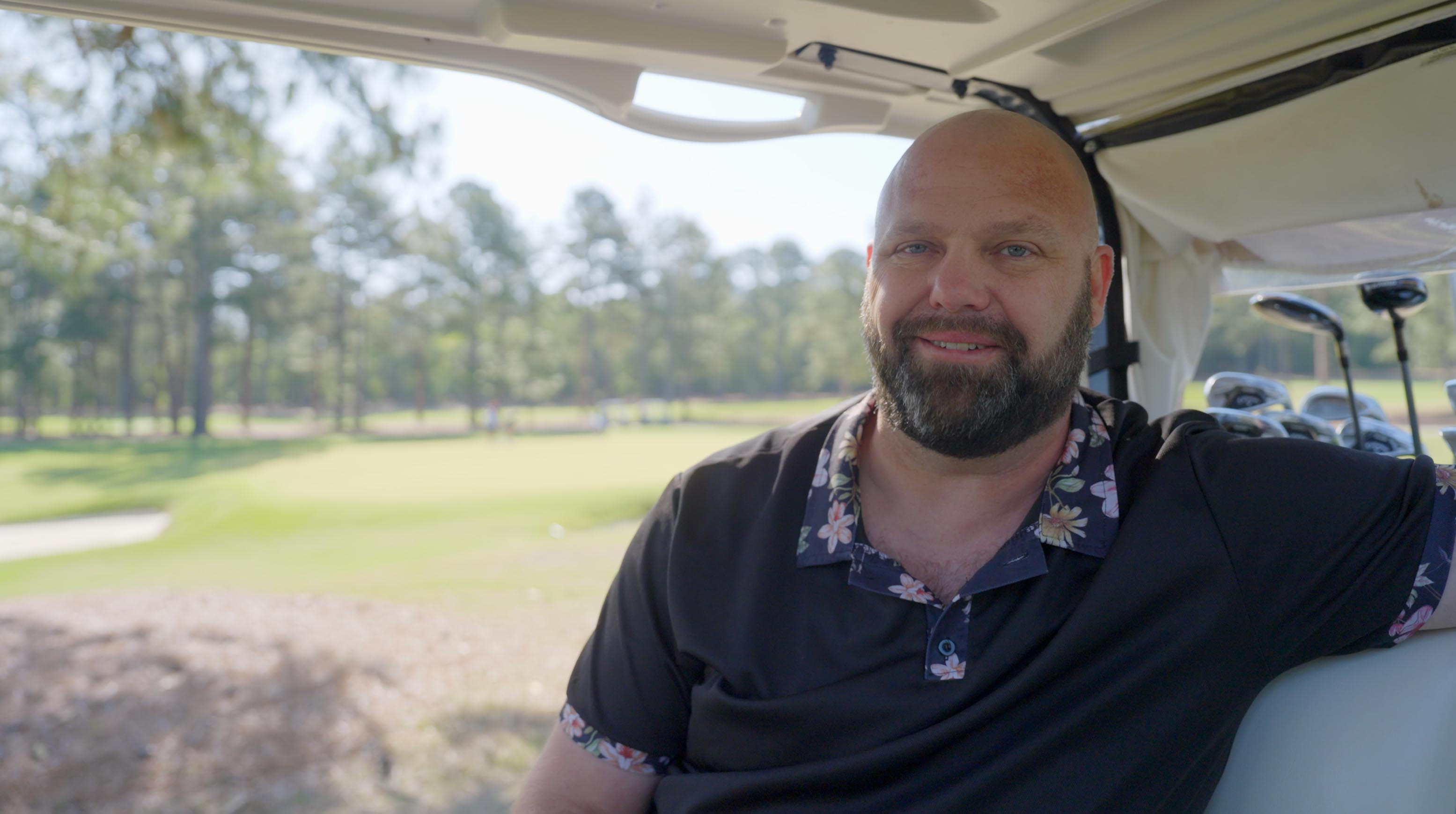 Man with a beard sitting in a golf cart on a sunny golf course