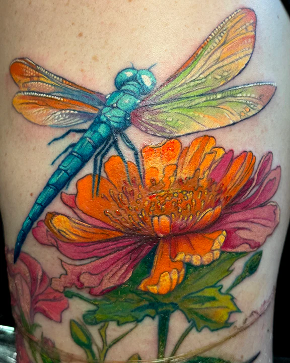 A bright, multi-colored tattoo of a turquoise dragonfly landing on a large orange and pink dahlia flower, characterized by soft color blending and realistic detail.