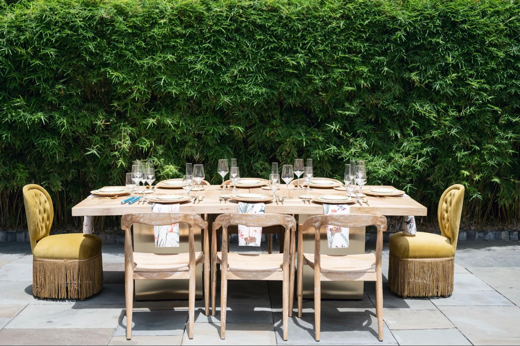 Elegant outdoor dining table with wood chairs, velvet end chairs, patterned runners, and luxury place settings.
