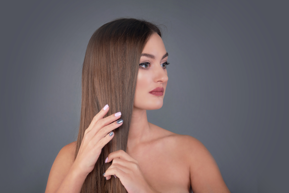 A young woman with smooth, sleek brown hair touching her strands to show the benefits of hair growth products and beef tallow for hair for shine and texture.