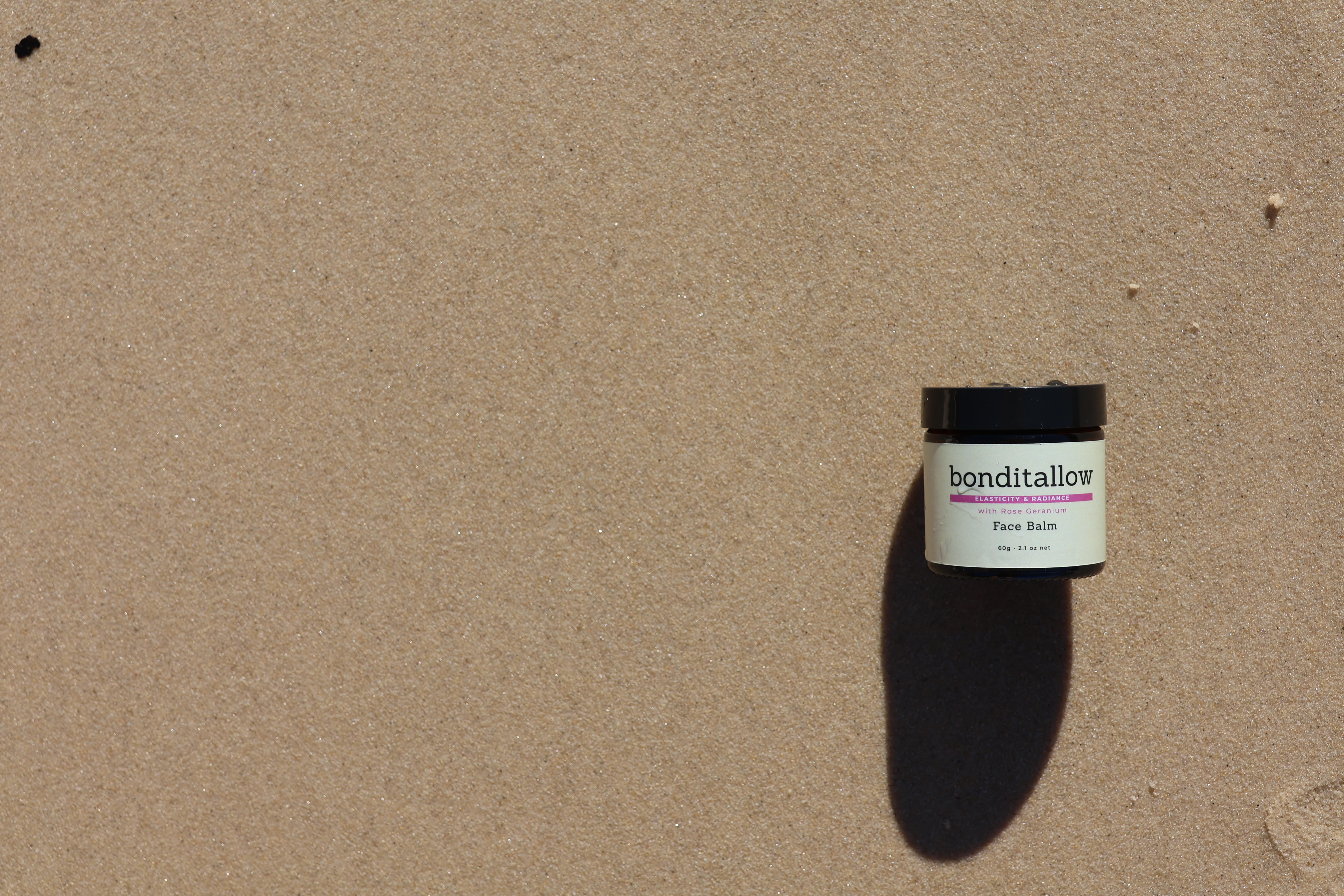 BondiTallow face balm jar on sandy beach surface