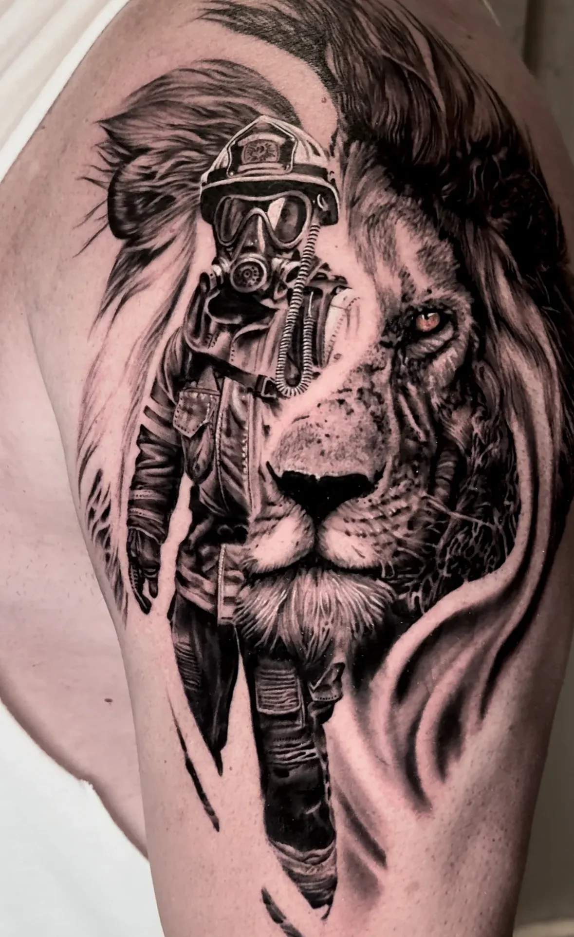 Detailed black and grey realism shoulder tattoo blending a firefighter and a lion's face.