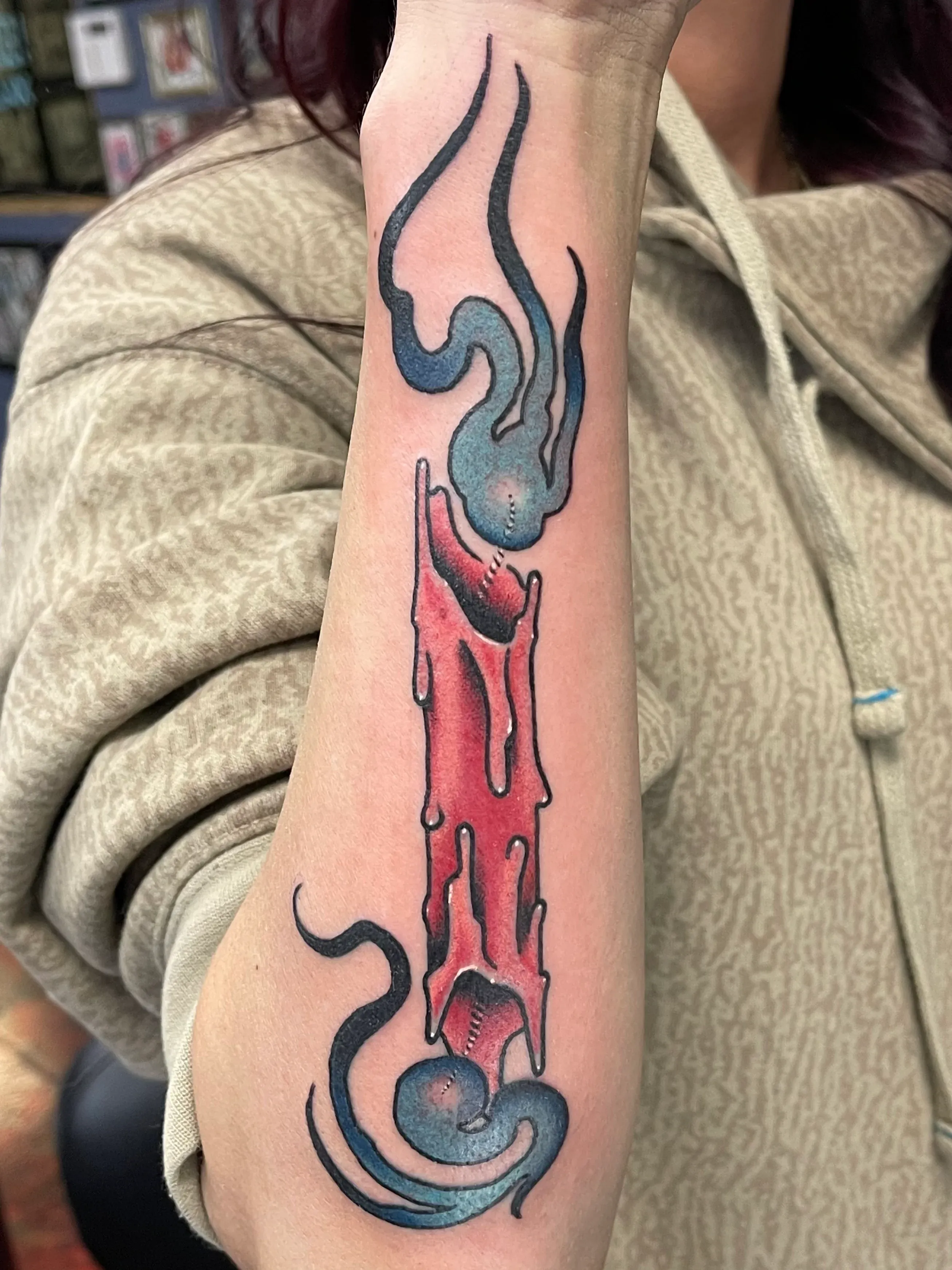 Forearm tattoo of a melting red candle with blue smoke swirling from the top and bottom.