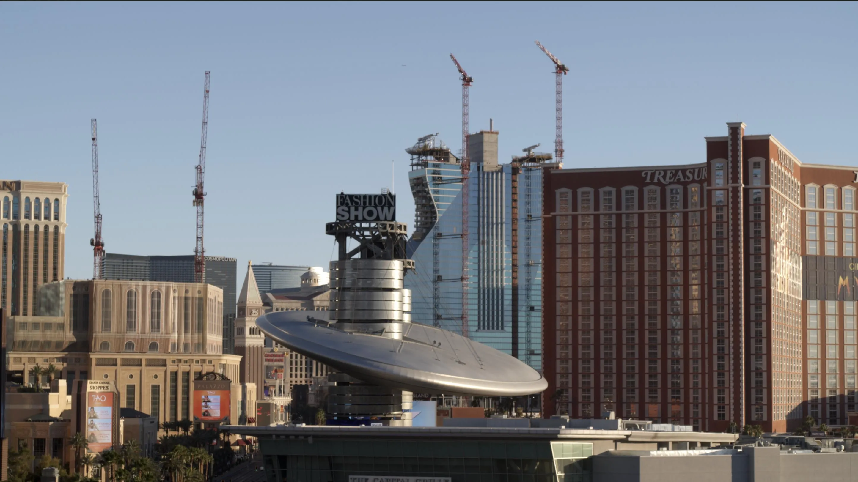 A sleek silver flying-saucer sculpture sits atop a building, with the Treasure Island resort and construction cranes visible building the Hard Rock Casino behind it.