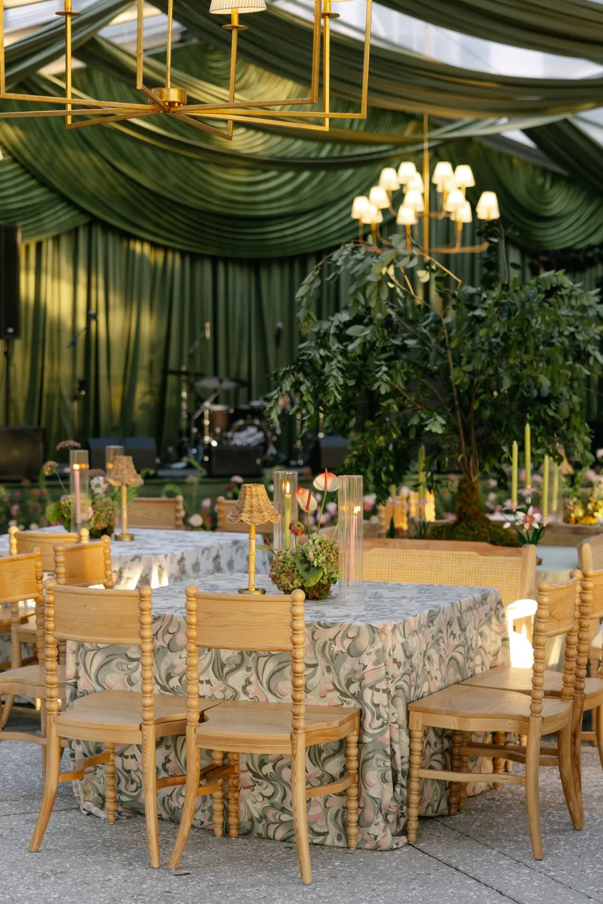 Rectangular event table with patterned linen, wood chairs, candlelight, and stage backdrop.