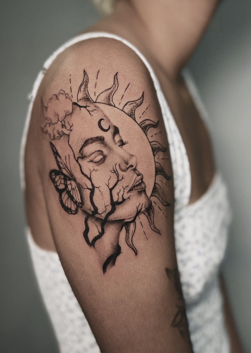 A black-and-grey illustrative realism tattoo on a shoulder cap depicting a woman's face seamlessly breaking apart into a stylized sun with radiant wavy rays and a delicate butterfly.