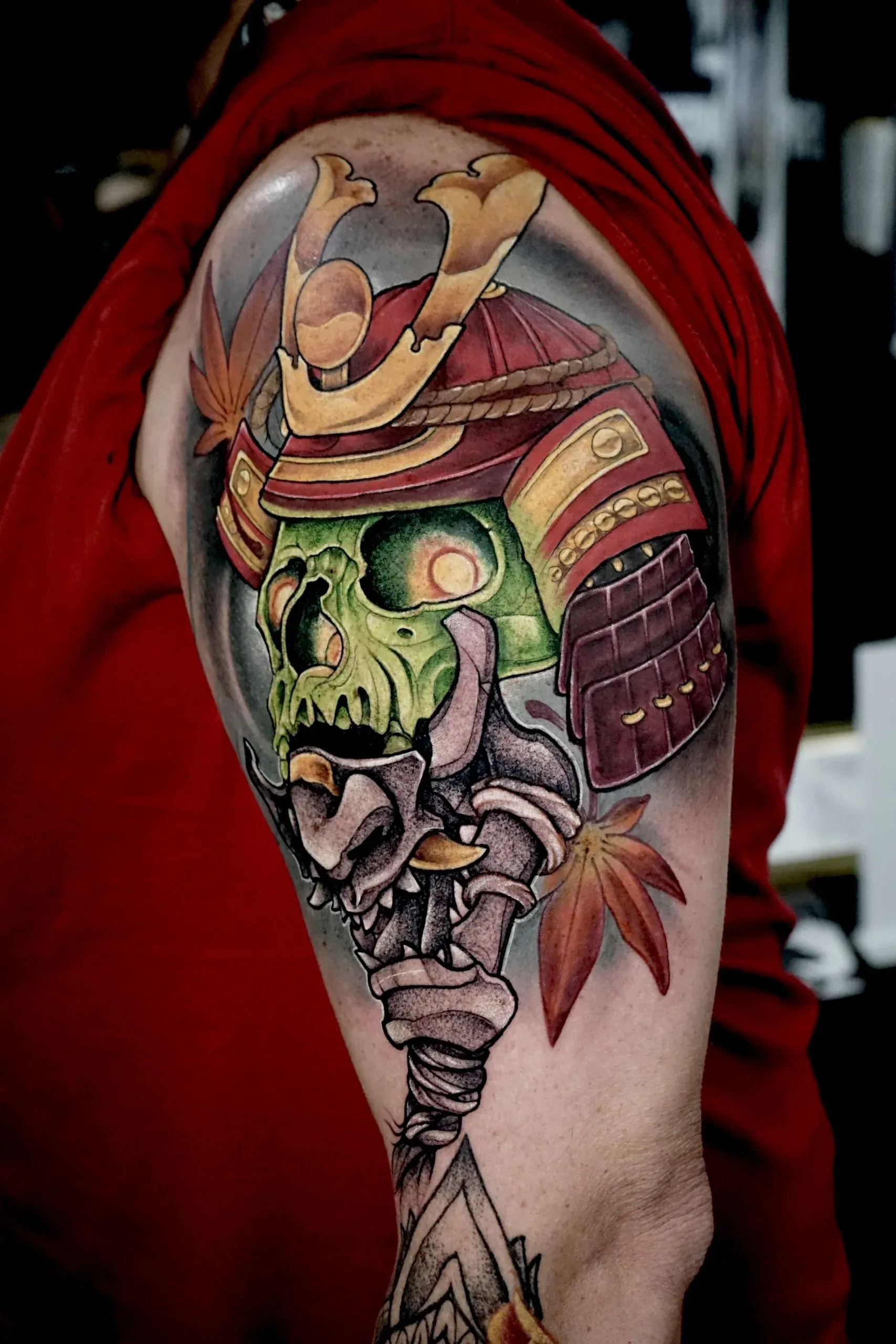 Colorful upper arm tattoo featuring a green skull wearing a red and gold Japanese samurai helmet.