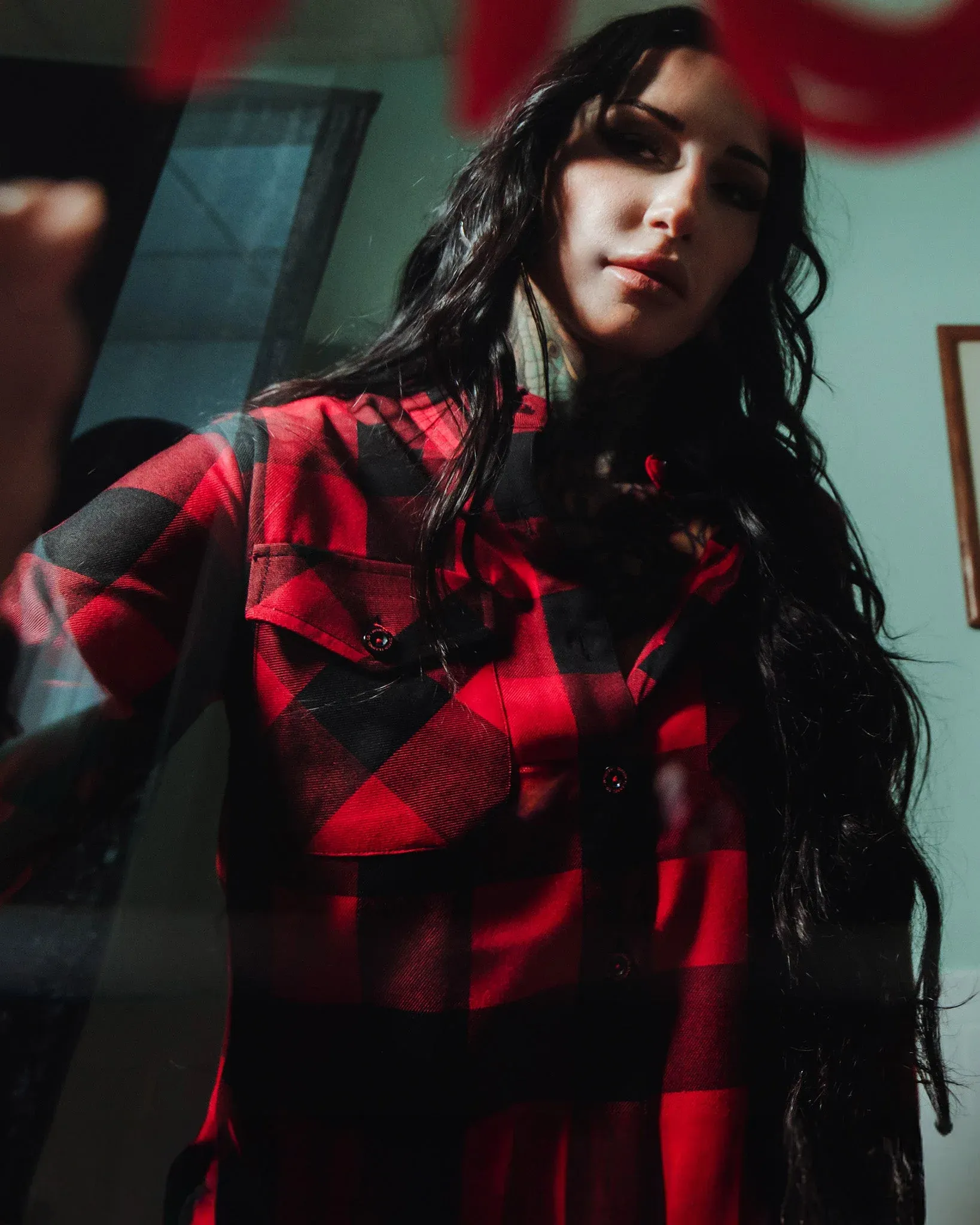 Woman wearing the Dixxon Redrum 10YR red and black plaid flannel shirt looking through a glass window.