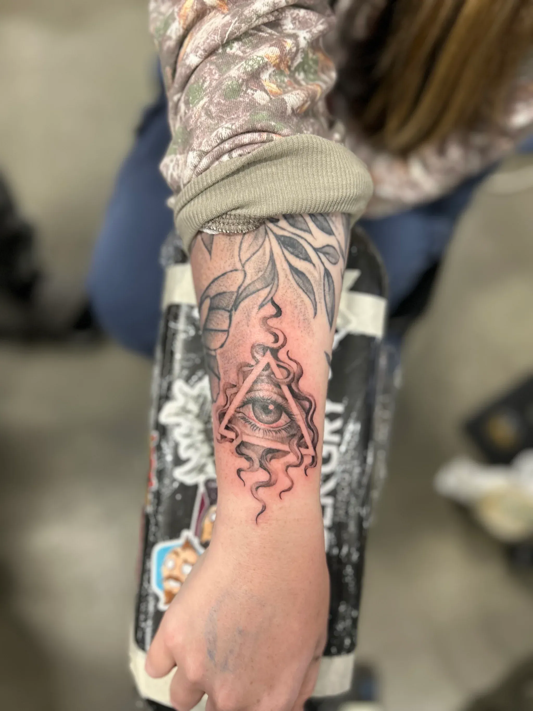 Eye of Providence triangle tattoo surrounded by wavy smoke lines on an inner forearm.