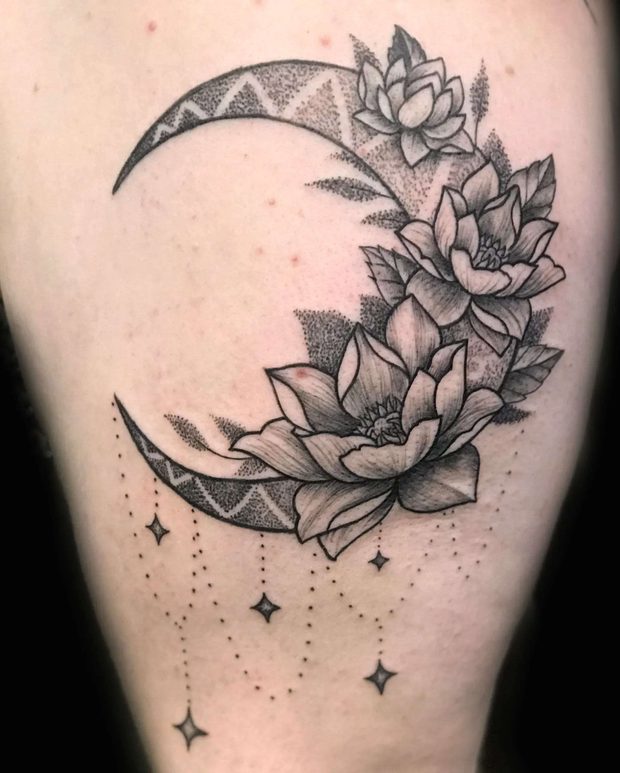 Black and grey stipple tattoo of a crescent moon adorned with lotus flowers and geometric patterns.