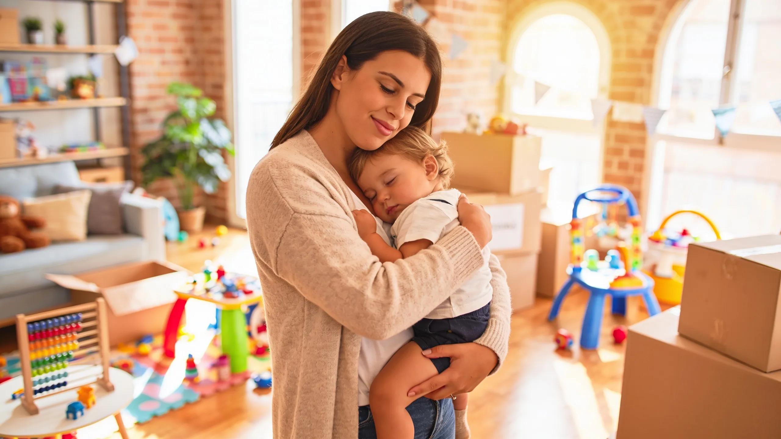 Family moving scene with parent carrying toddler in a warm living room filled with moving boxes