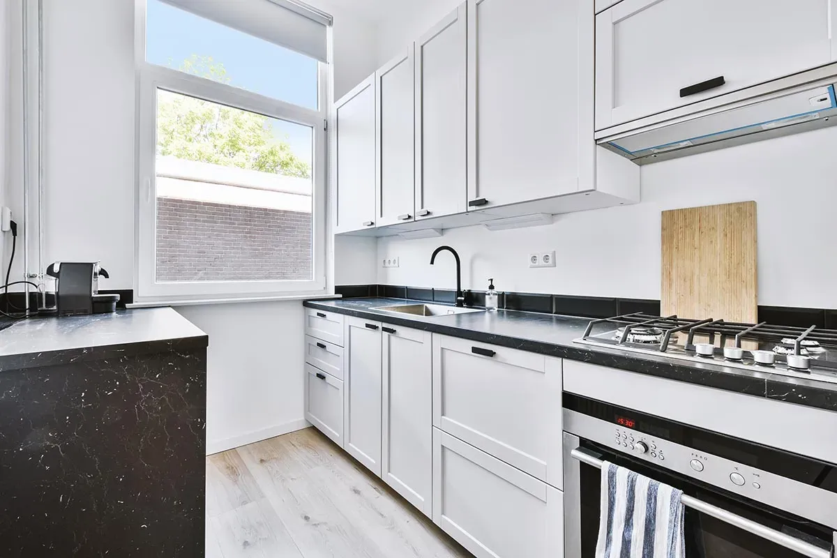 What Are The Best Cabinet Styles for Small Kitchens in Savannah Modern kitchen with white cabinetry, black countertops, and a window