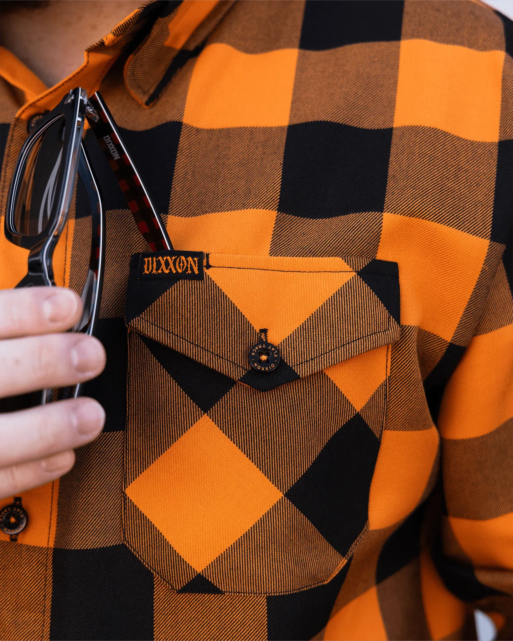 Dixxon orange and black buffalo check flannel with sunglasses tucked into the chest pocket.