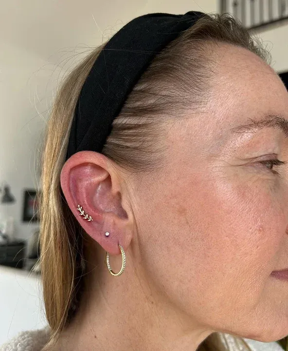 Gold ear piercings with a leaf flat cartilage stud, a lobe stud, and a small gold hoop earring.