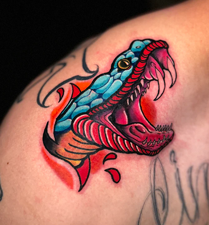 A vibrant, colorful tattoo of an open-mouthed snake head. The design features bright blue scales, a deep pink mouth with sharp white fangs, and orange and red highlights, rendered in a bold neo-traditional style.