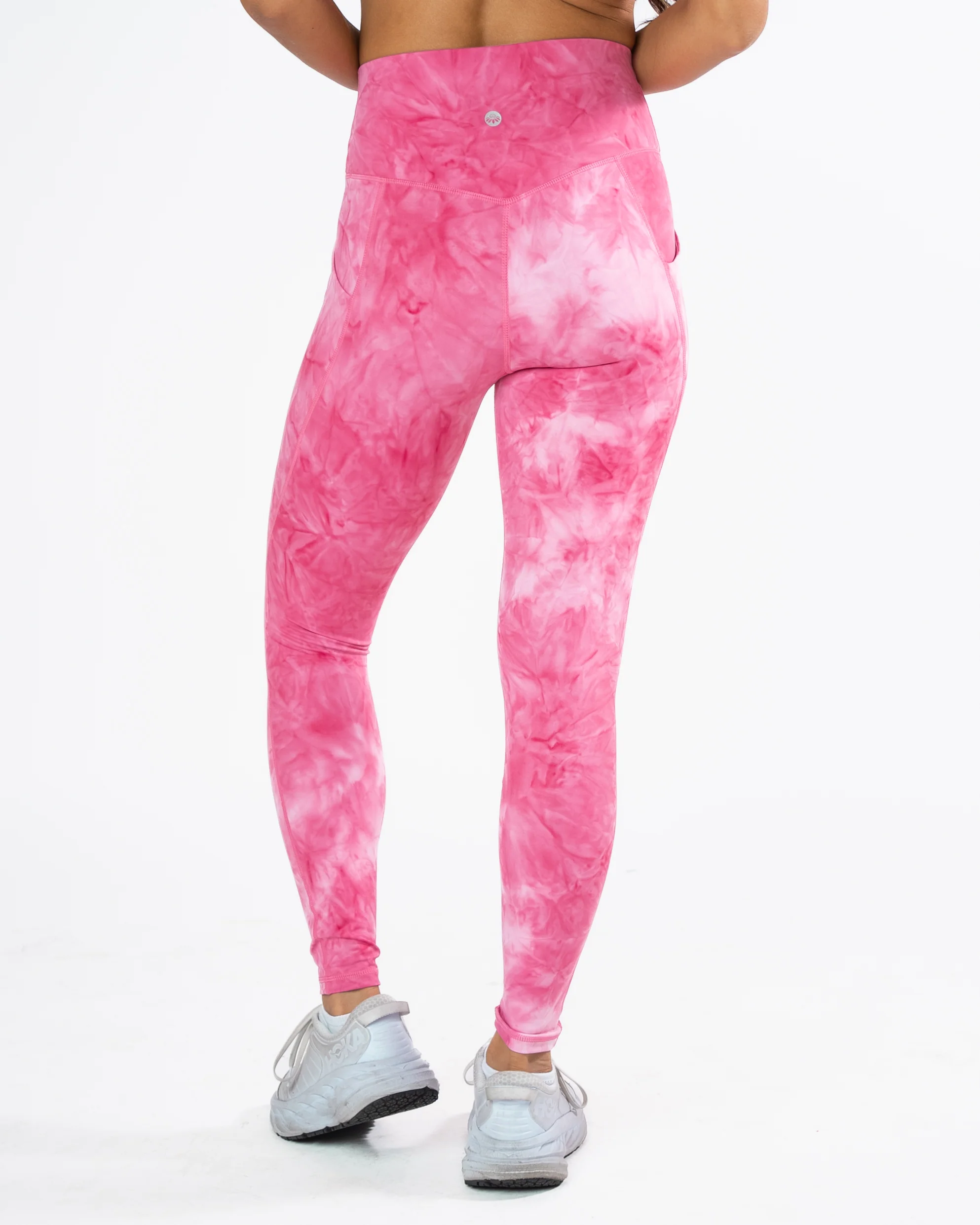 Rear view of high-waisted athletic leggings featuring a pink and white hibiscus tie-dye pattern, complete with an athletic V-shaped back waistband seam, subtle logo detail, and side pockets.