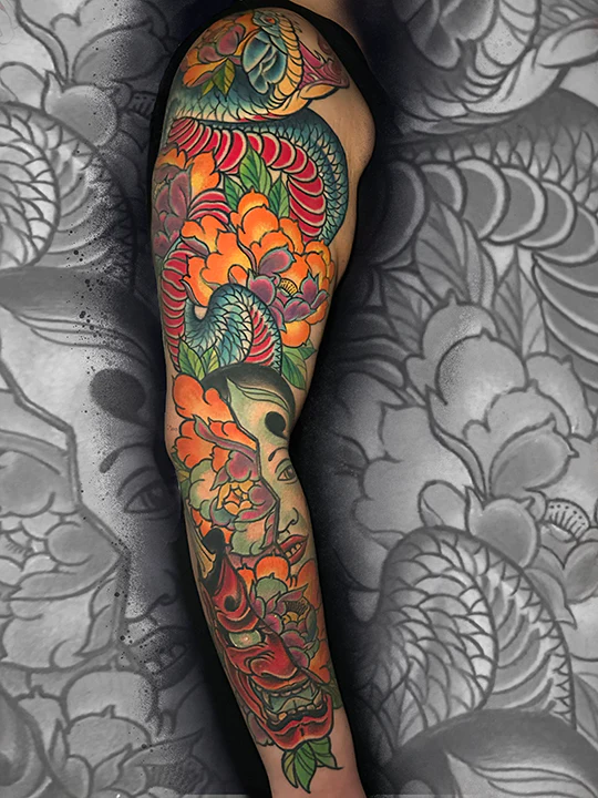 A full-sleeve Japanese Irezumi style tattoo featuring a colorful dragon weaving through vibrant orange chrysanthemums, peonies, and a traditional Japanese theater mask