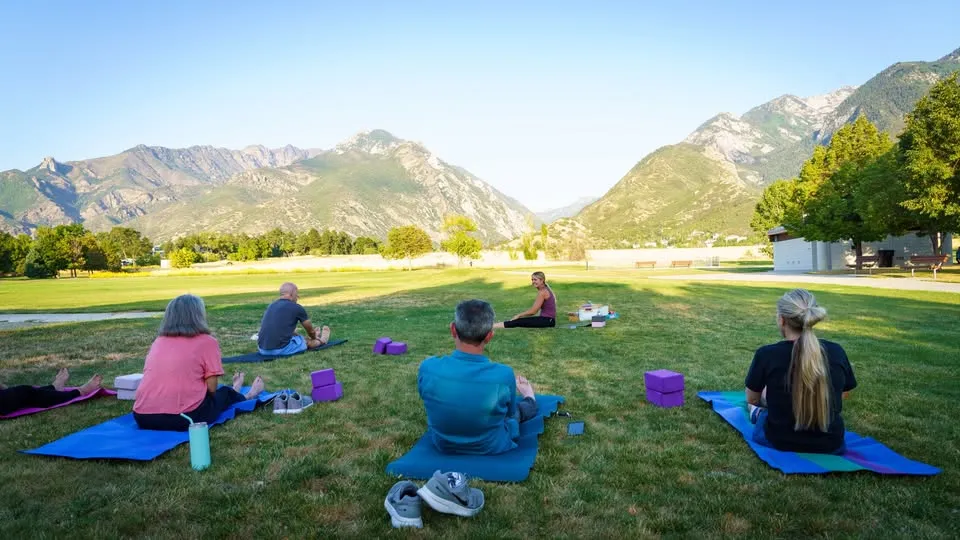 Group yoga session on grass, surrounded by mountains and trees