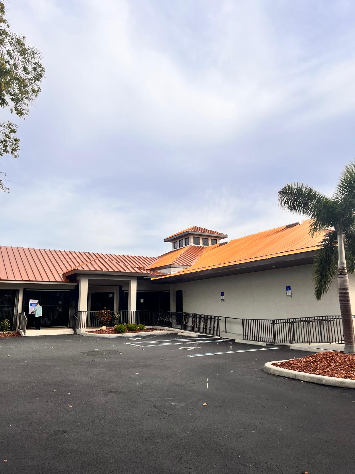 Florida commercial building with a metal roof under a partly cloudy sky and surrounding landscaping.