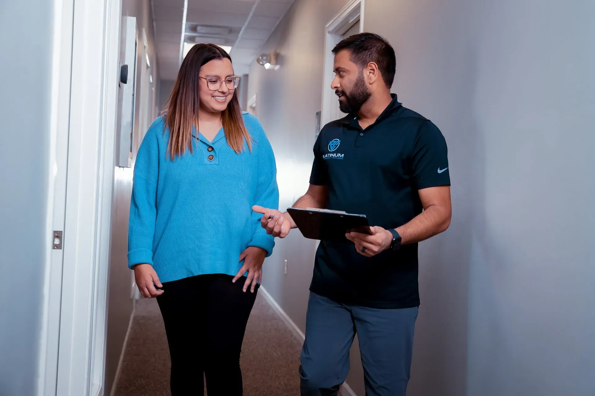 Two people walking down a hallway, discussing while one holds a tablet