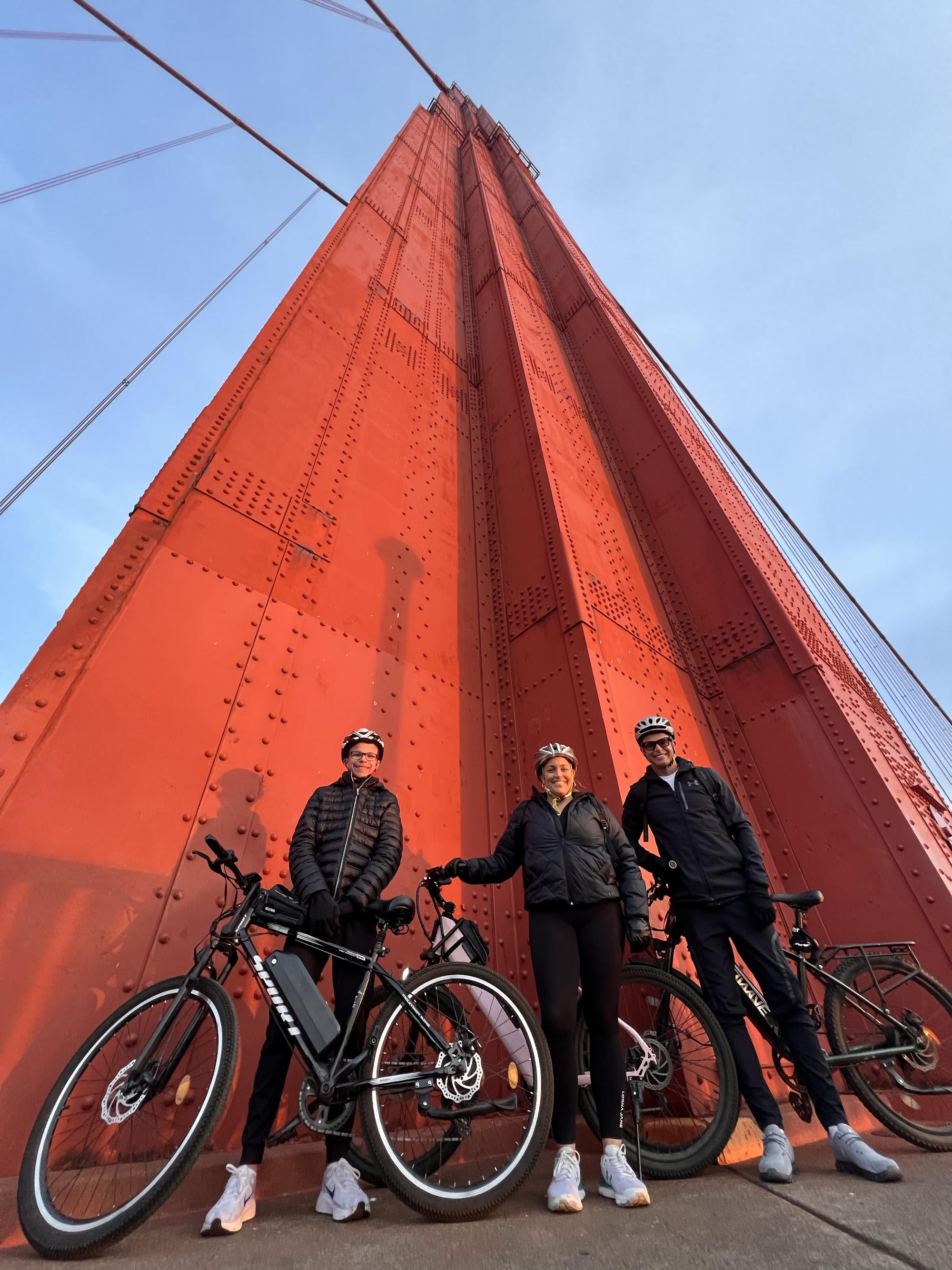 Three cyclists posing in front of a red bridge tower