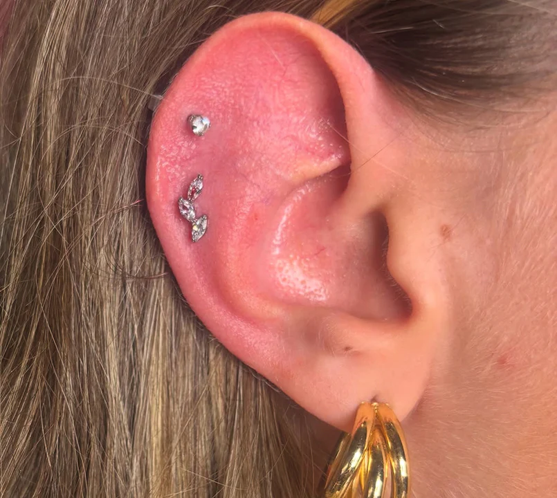 Close-up of a curated ear project showcasing a flat helix piercing with a crystal cluster piece paired with chunky gold lobe hoops