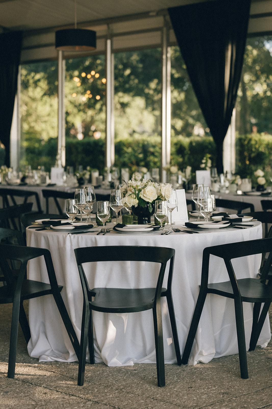 Round event table with white linen, black chairs, glassware, and white floral centerpiece.