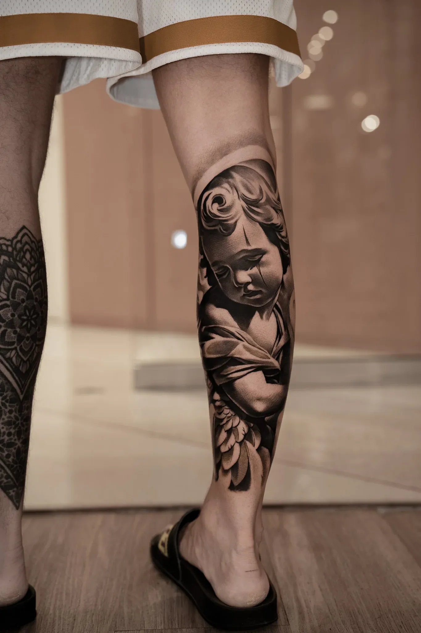 Detailed black and grey realism calf tattoo depicting a weeping cherub angel with a tear on its cheek.
