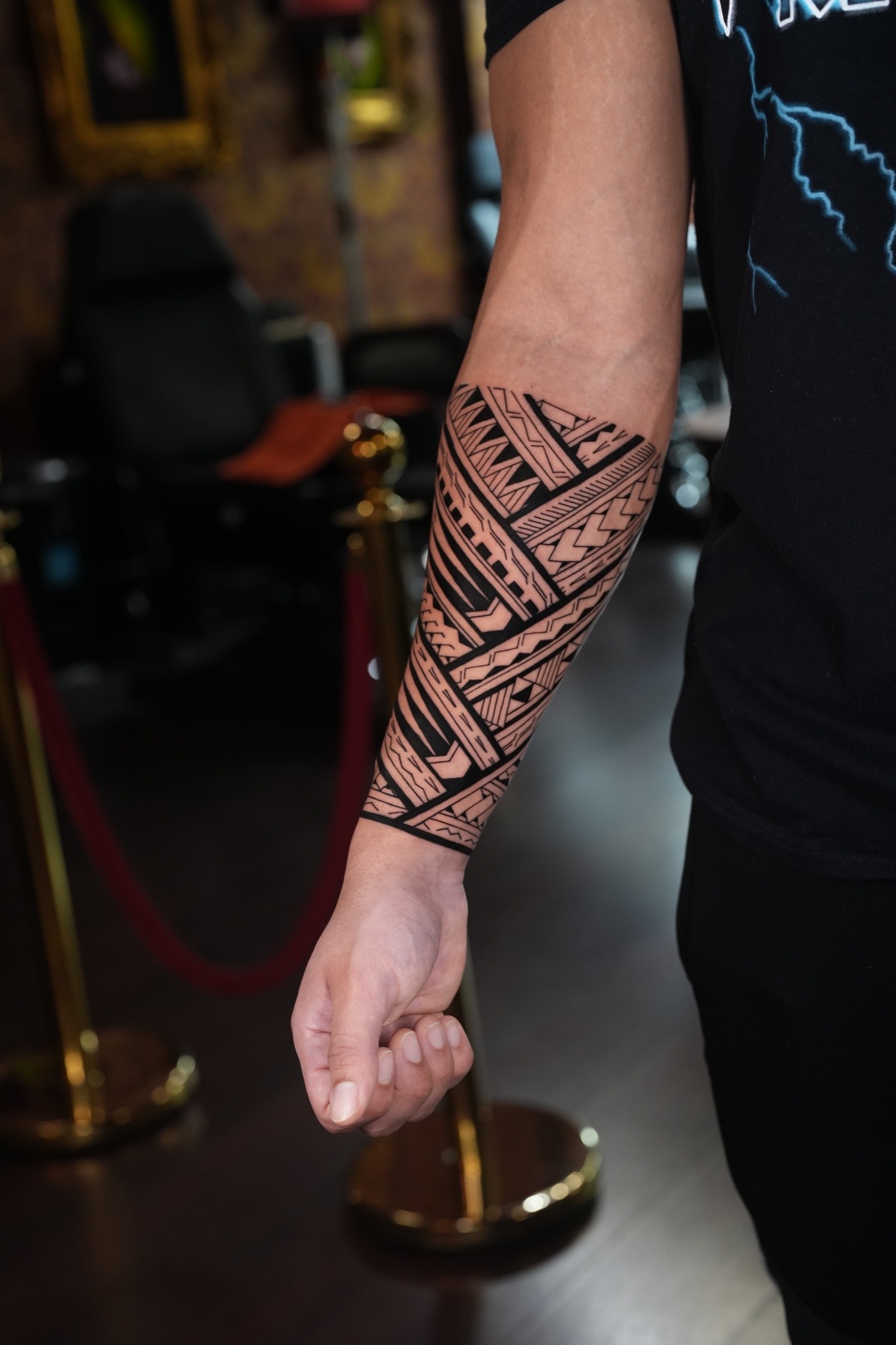 A bold blackwork geometric forearm tattoo band featuring overlapping Polynesian-inspired patterns, triangles, and clean parallel line work