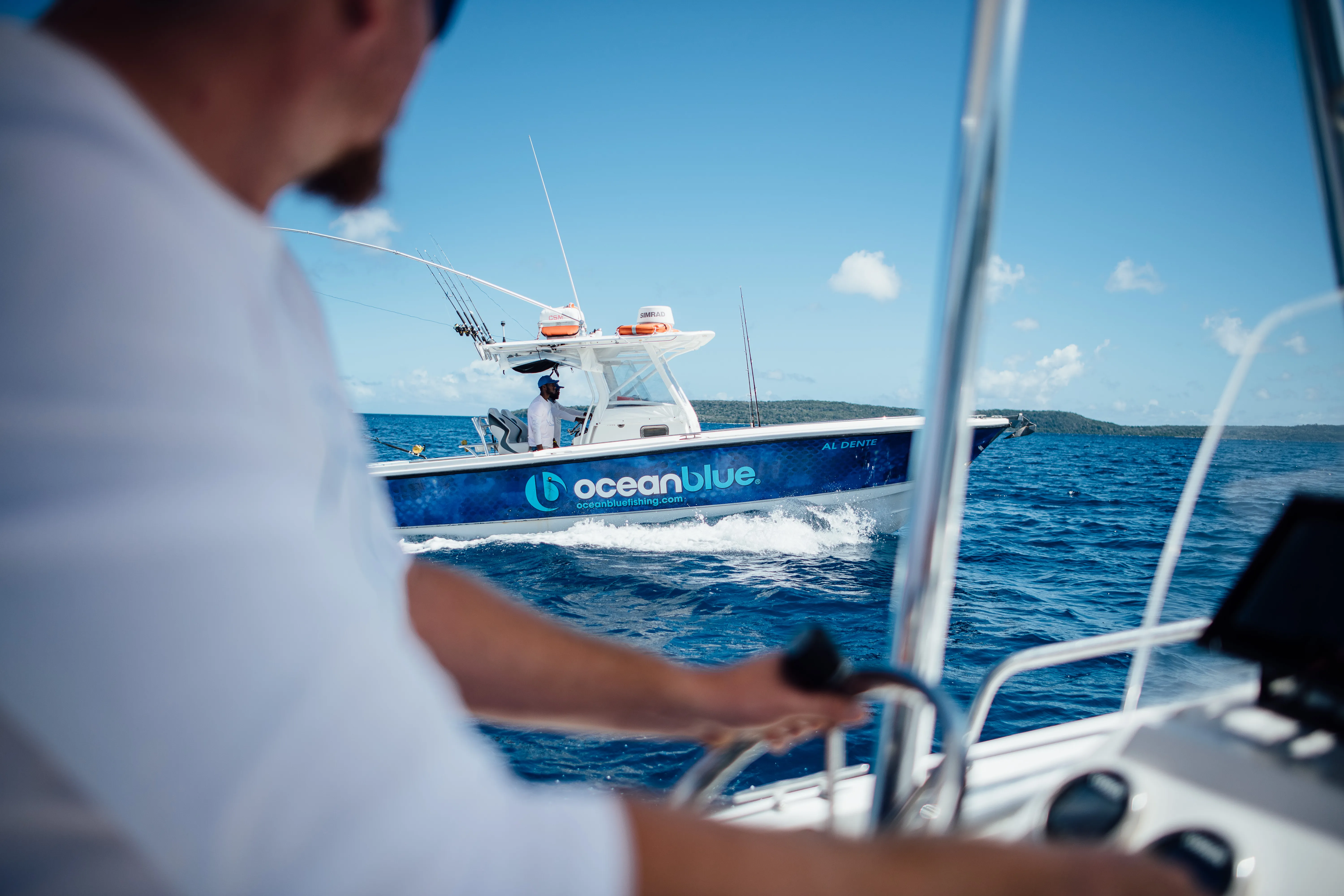 Ocean Blue Fishing Adventures centre-console boat cruising on blue water in Vanuatu, viewed from another boat with a skipper in the foreground.