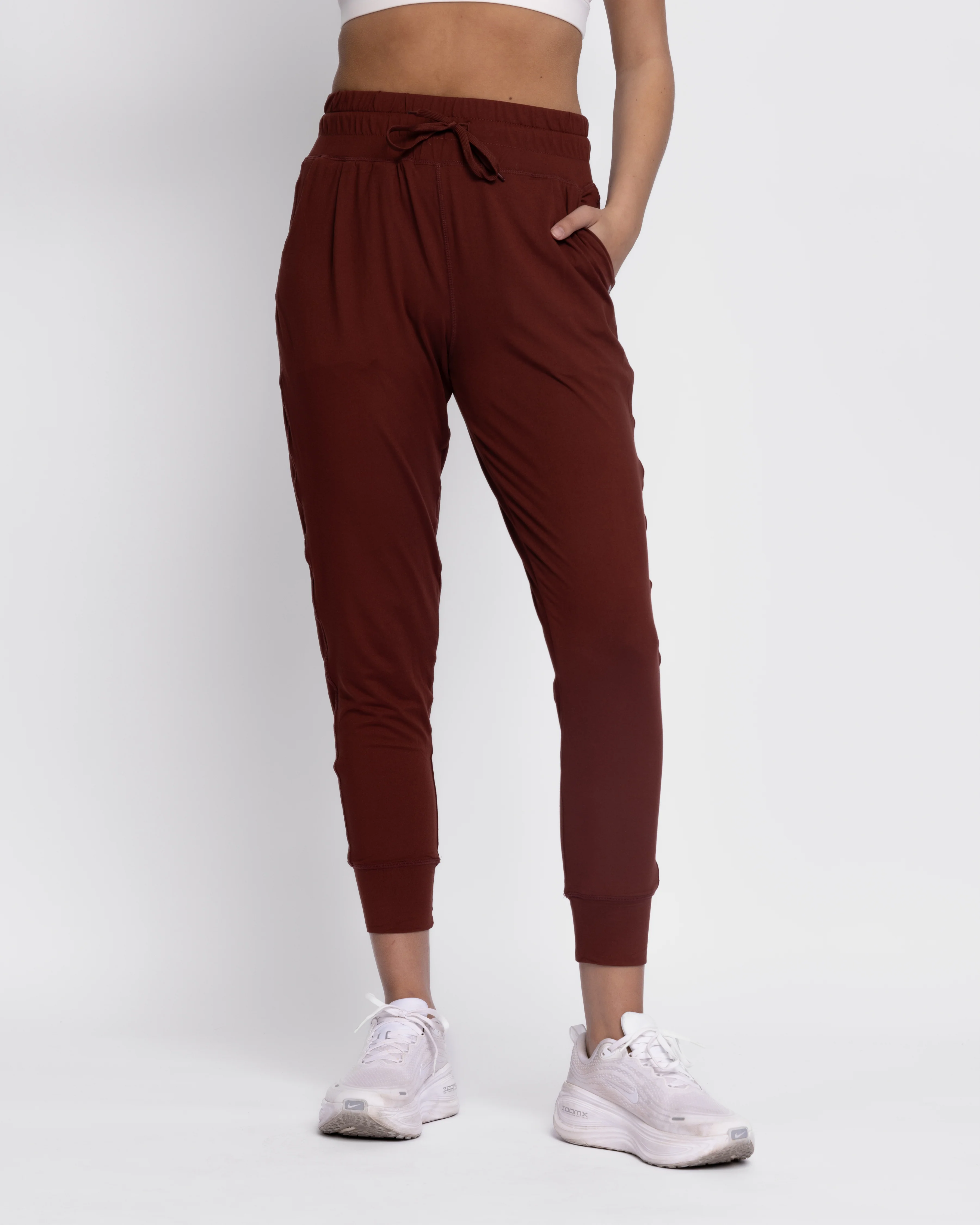 A front-facing product view of a model wearing Senita lightweight, relaxed-fit joggers in a rich chocolate brown shade, showcasing the flexible elastic drawstring waistband, cozy side pockets, and tapered ankle cuffs.