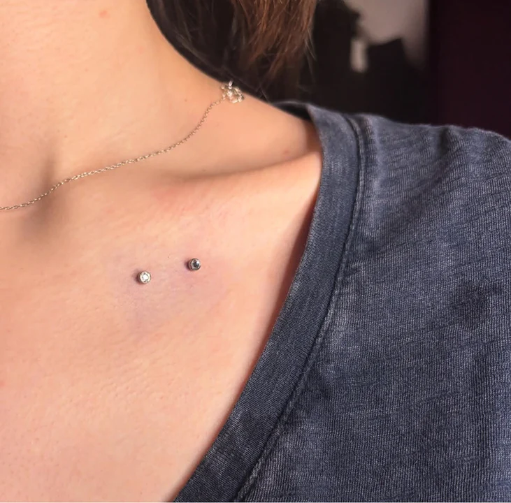 Close-up of a fresh double dermal anchor piercing placed elegantly along a woman's collarbone using minimalist silver crystal studs