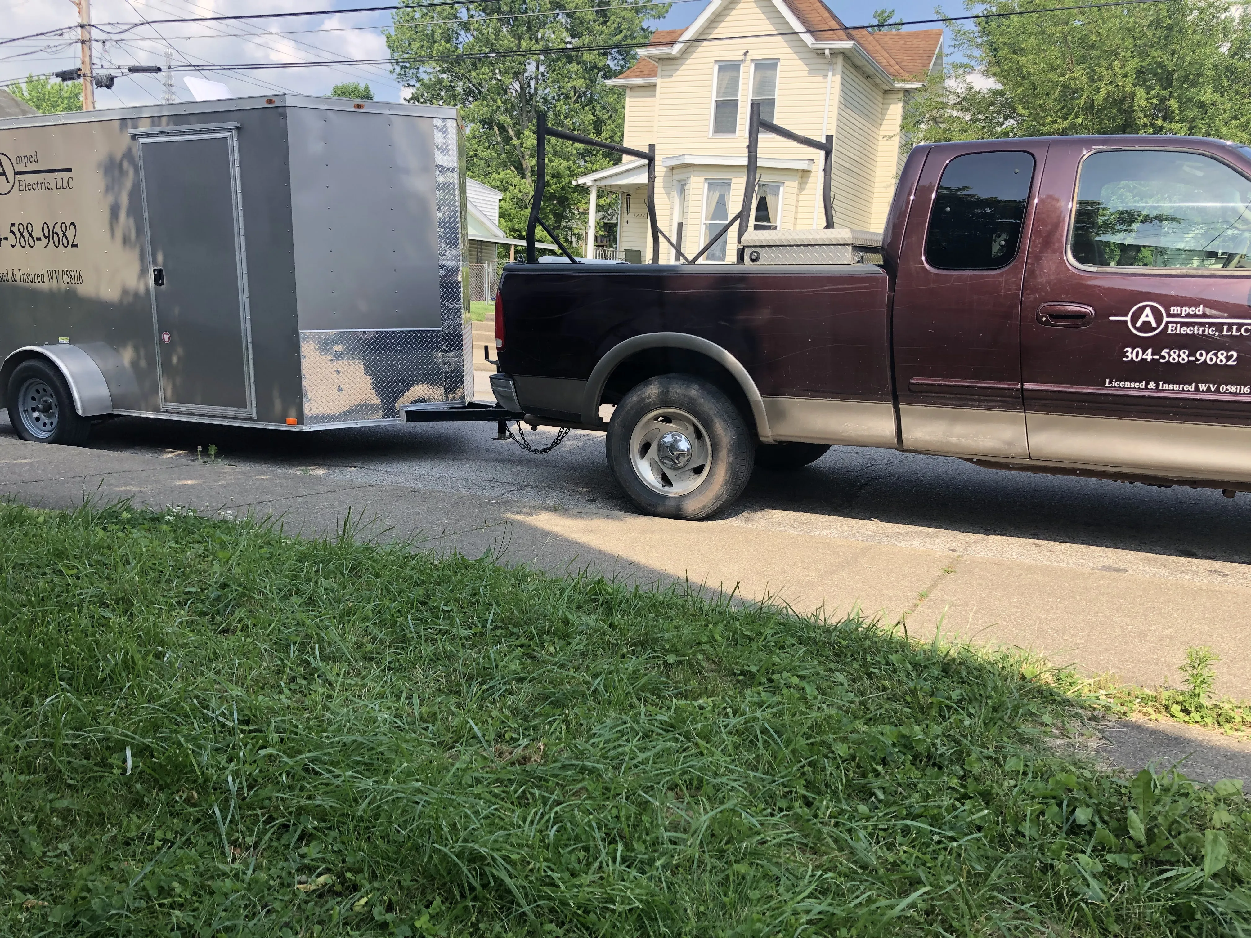 Amped Electric LLC branded maroon truck and silver enclosed trailer parked on a residential street in West Virginia