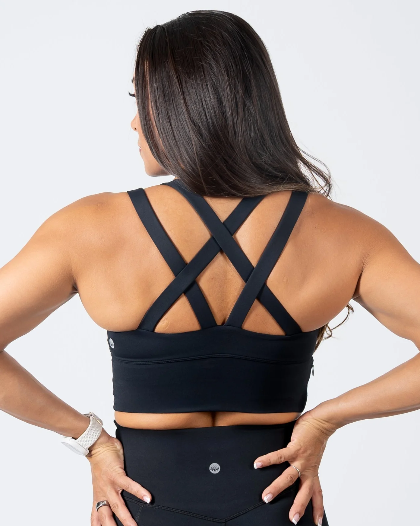 Back view of a woman showcasing a black sports bra with an intricate criss-cross strappy back design and a wide, supportive band.