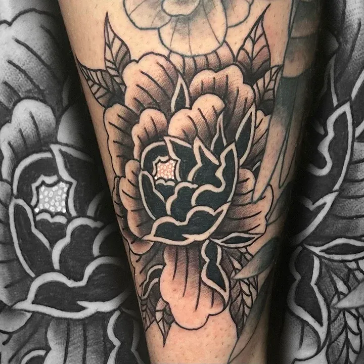 Black and grey traditional flower tattoo with bold outlines and shaded petals on a forearm.