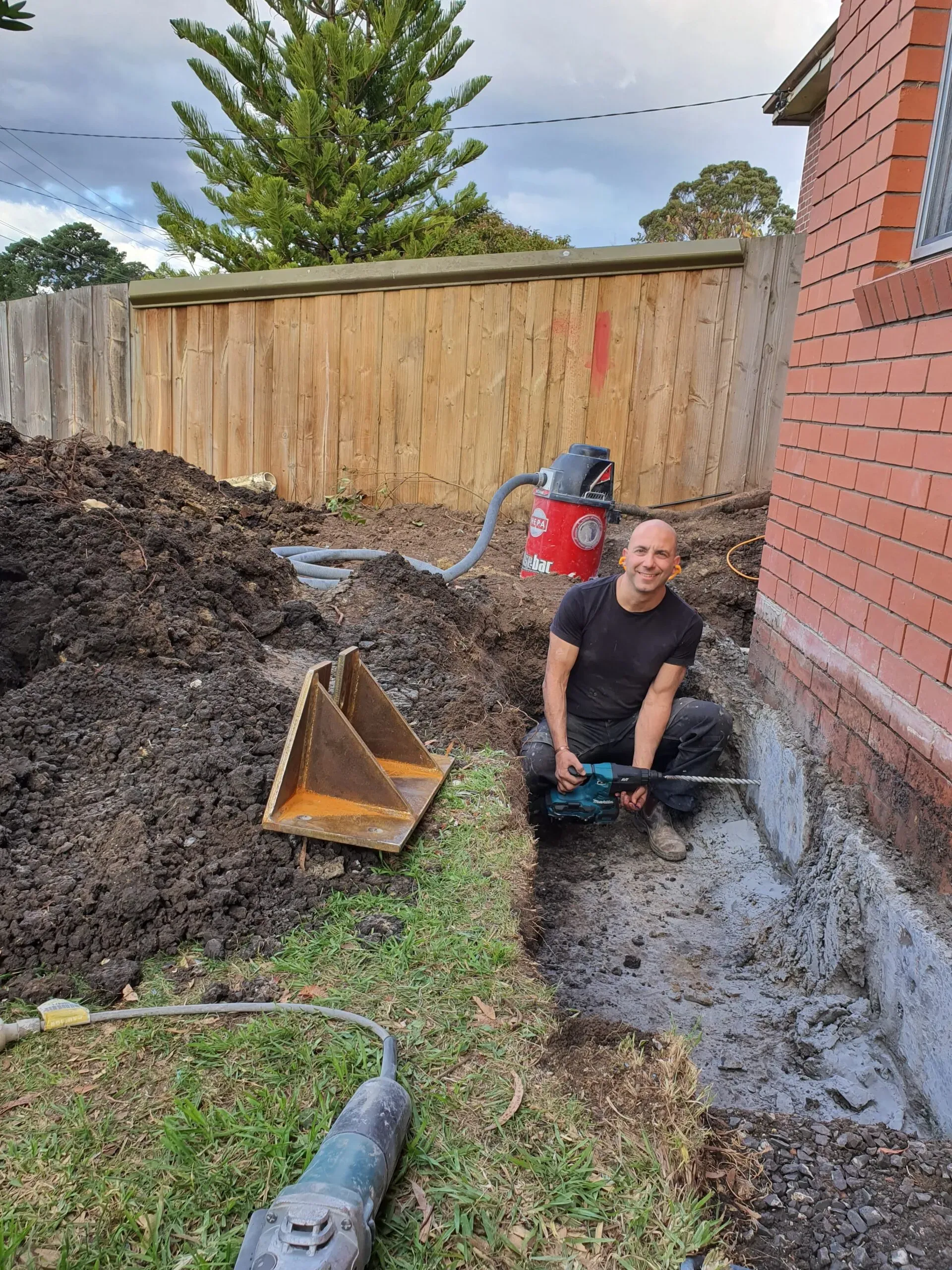 Contractor using screw pile underpinning equipment at a foundation repair site