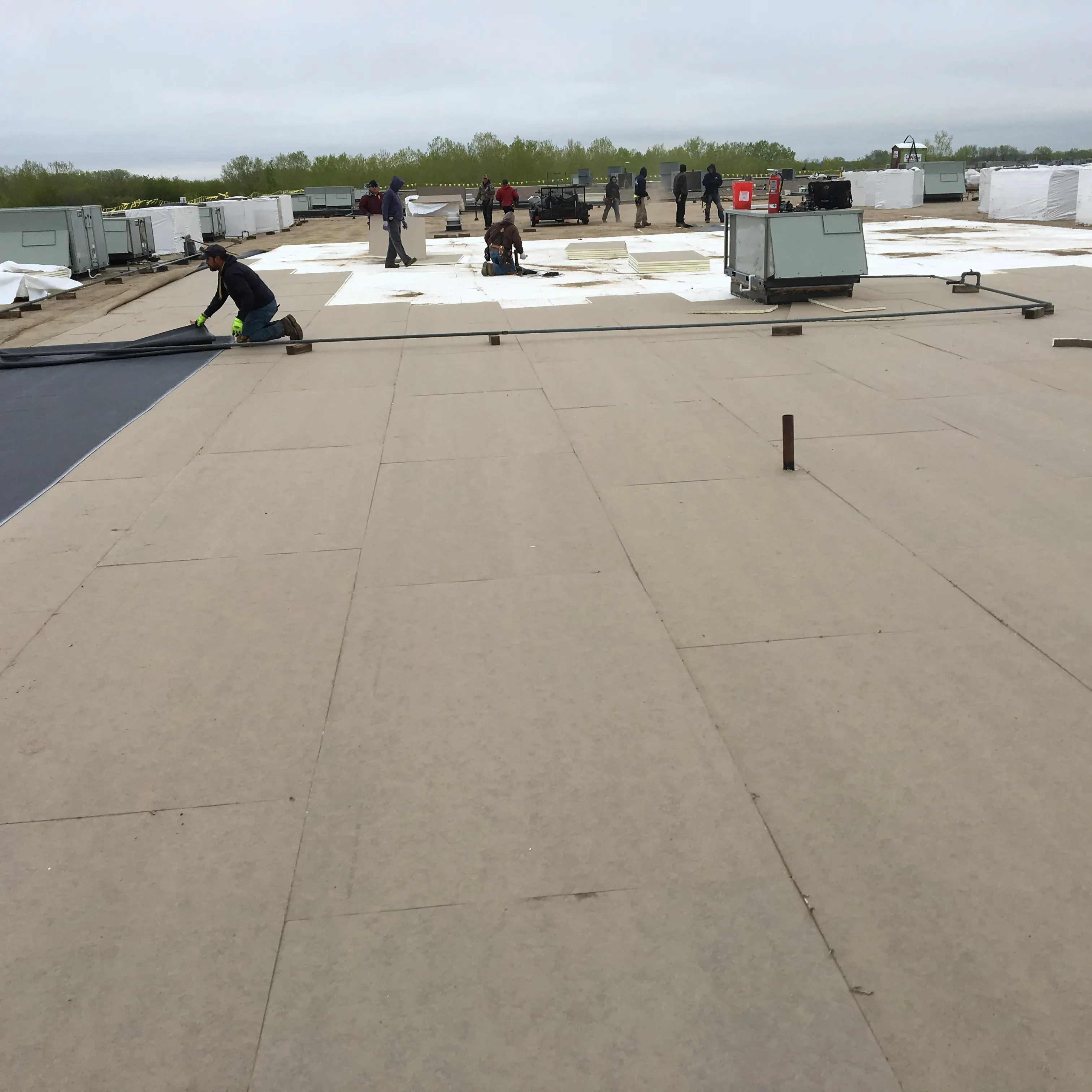 Workers installing roofing materials on a large flat rooftop