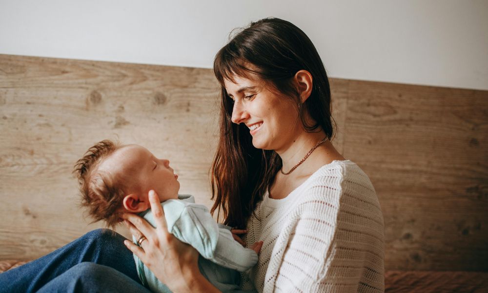 A smiling mother holding her newborn baby, considering whether natural balms like tallow for skin are better for skin conditions like diaper rash or infant eczema.